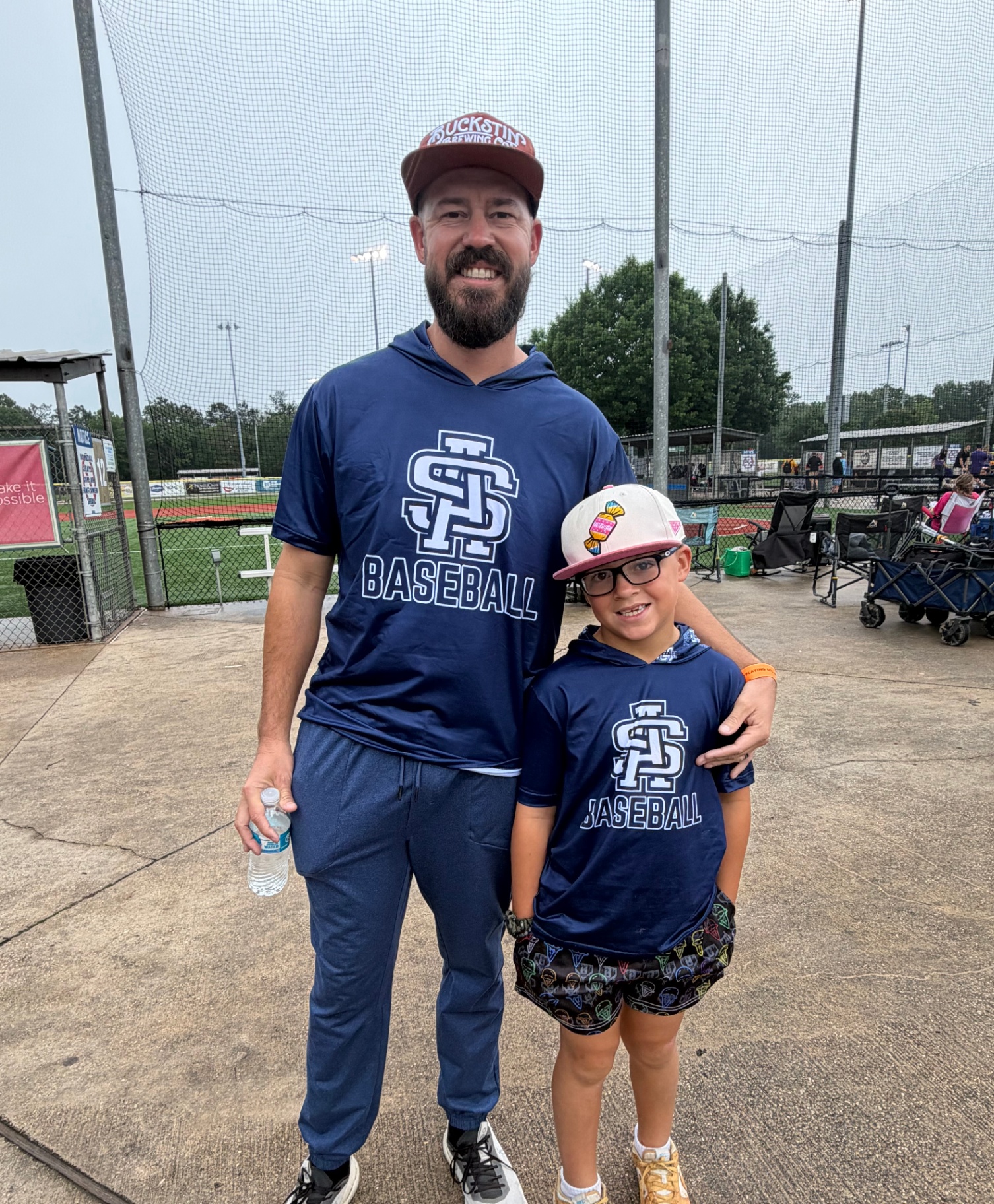 Dad and son at the ballpark in matching SP Baseball gear and Parish Culture shorts